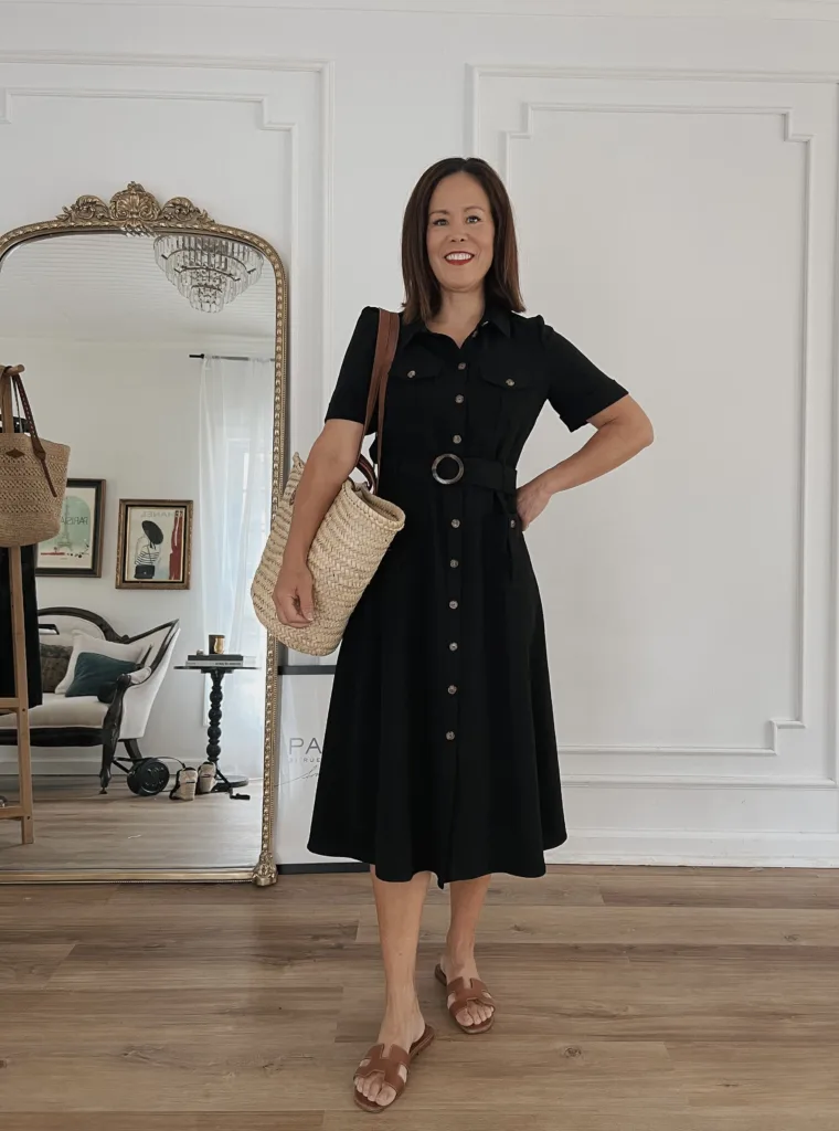 Woman wearing black dress with brown sandals and market bag.