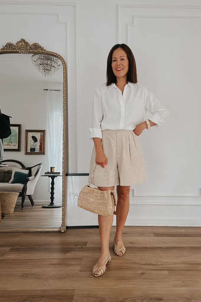 Lady wearing white linen top, linen shorts, raffia bag and gold sandals.