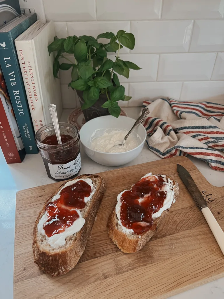 Two pieces of toast with ricotta and jam on a wooden cutting board.