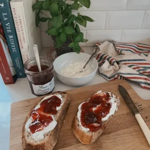 Two pieces of toast with ricotta and jam on a wooden cutting board.