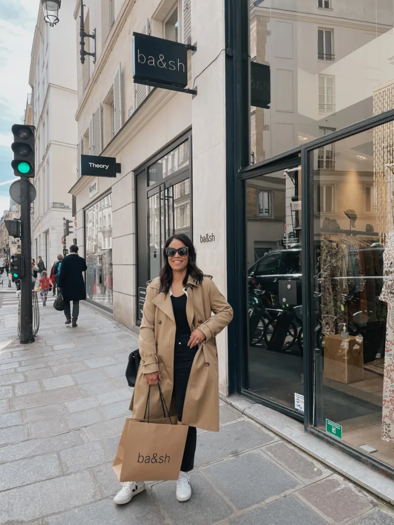 Women in trench coat holding bag in front of bash paris.