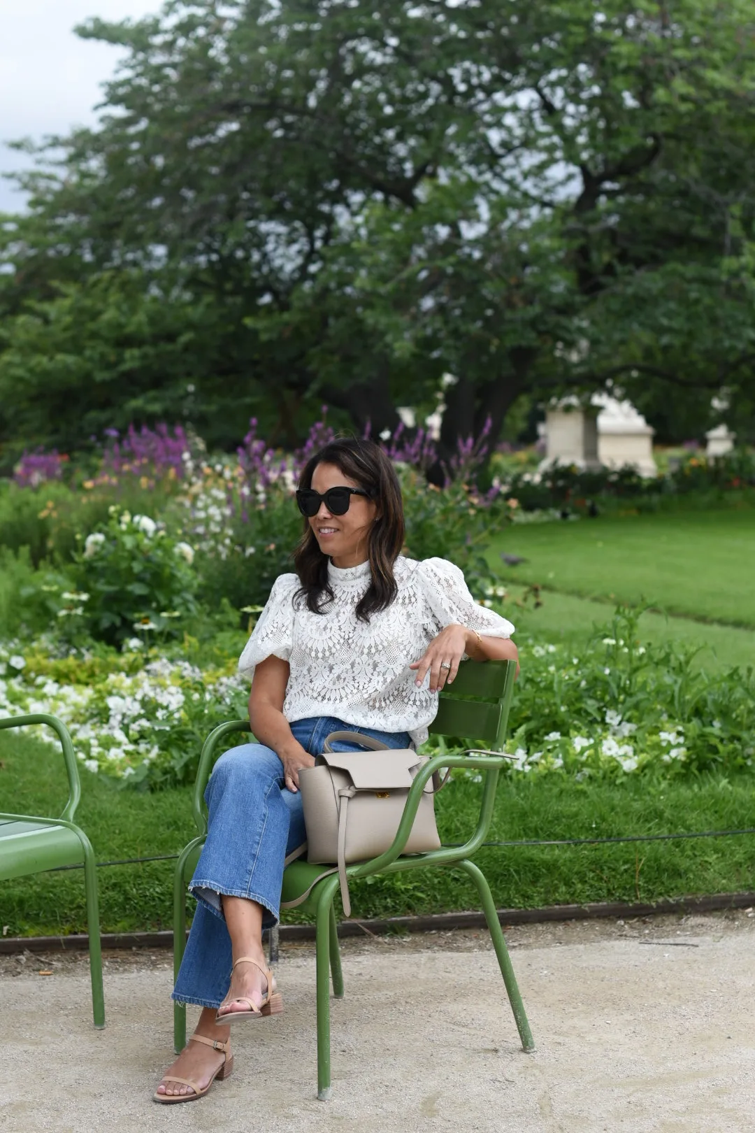 Woman sitting in green chair in Paris with eyelet top.