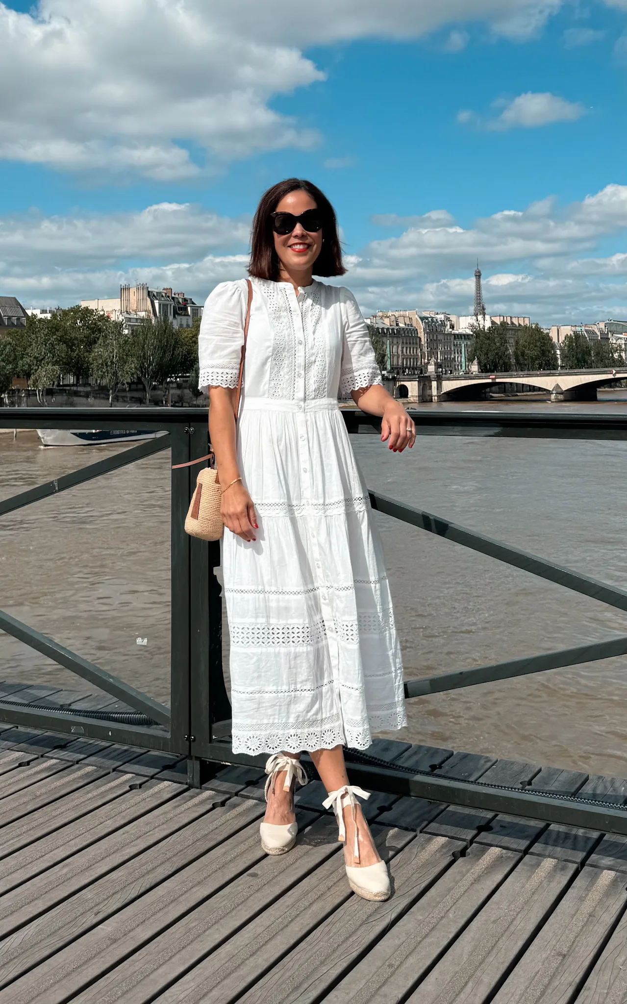 Woman wearing white dress walking across bridge.