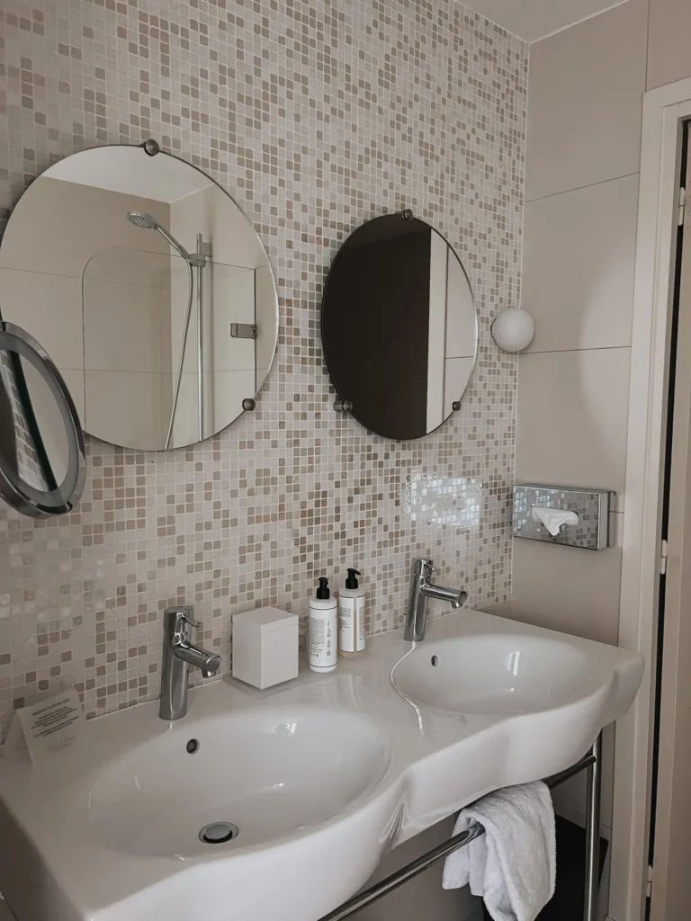 Hotel des Saint Pères | Interior of a bathroom with 2 circular mirrors and 2 sinks.