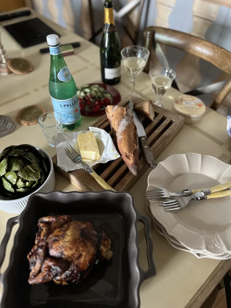 roasted chicken, wine bottle, artichoke sitting on a table.