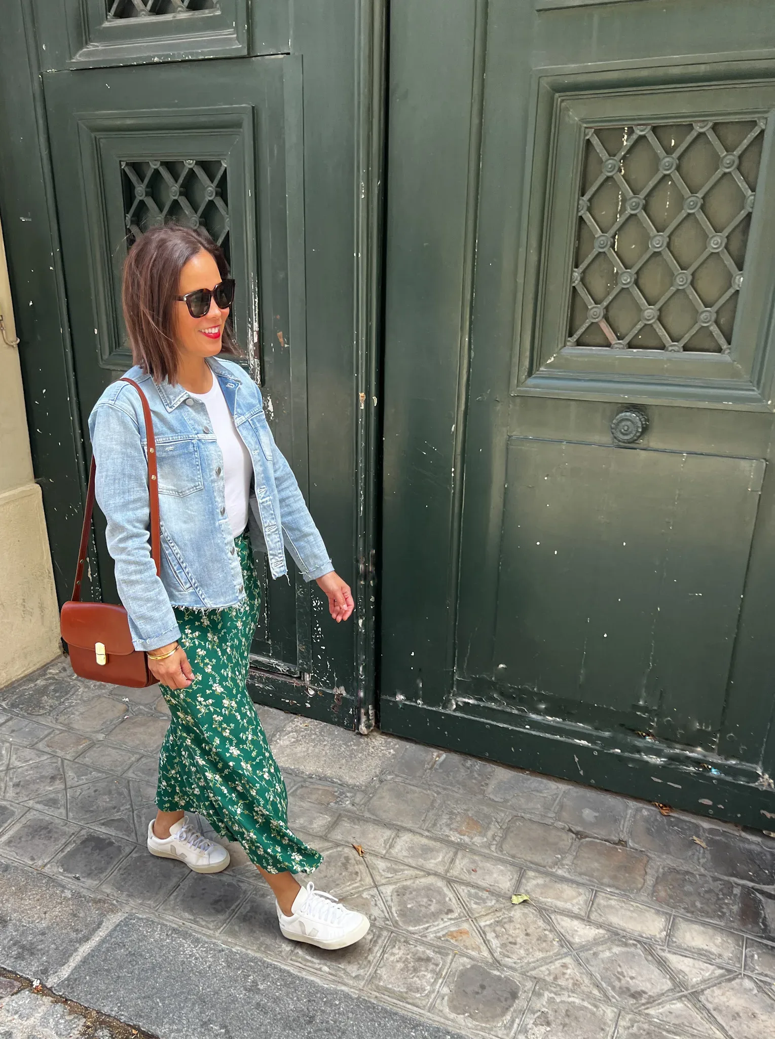 Woman wearing floral green skirt with denim jacket and sneakers while walking