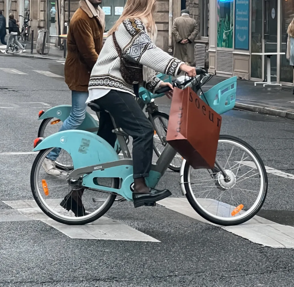 Woman riding bike wearing black loafers and sweater in Paris.