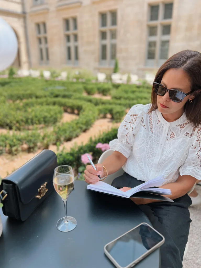 Woman sitting down to write wearing white eyelet top.
