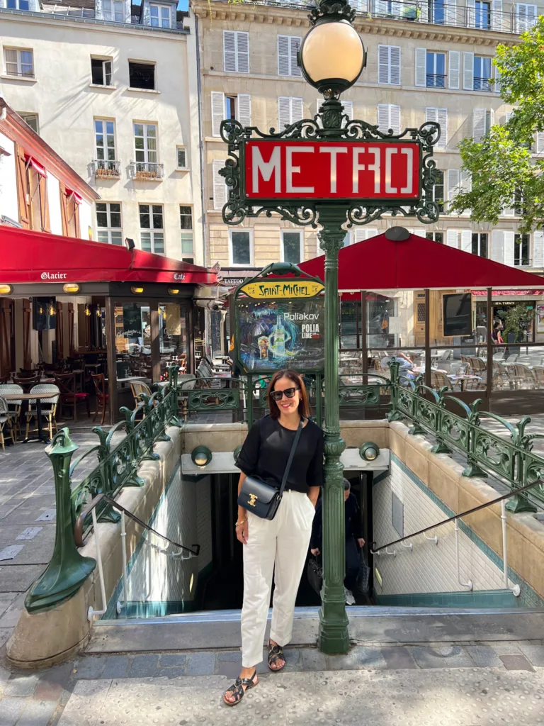 Woman standing against a metro sign wearing pants and a black shirt.