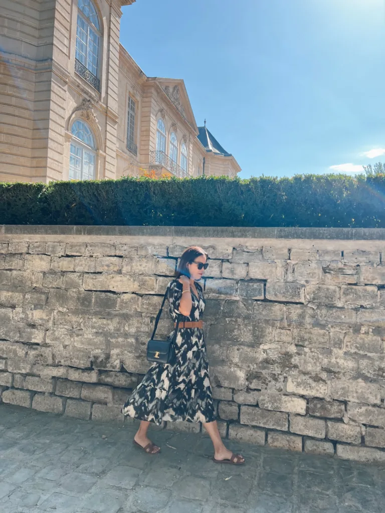 Woman walking by a wall wearing black dress.