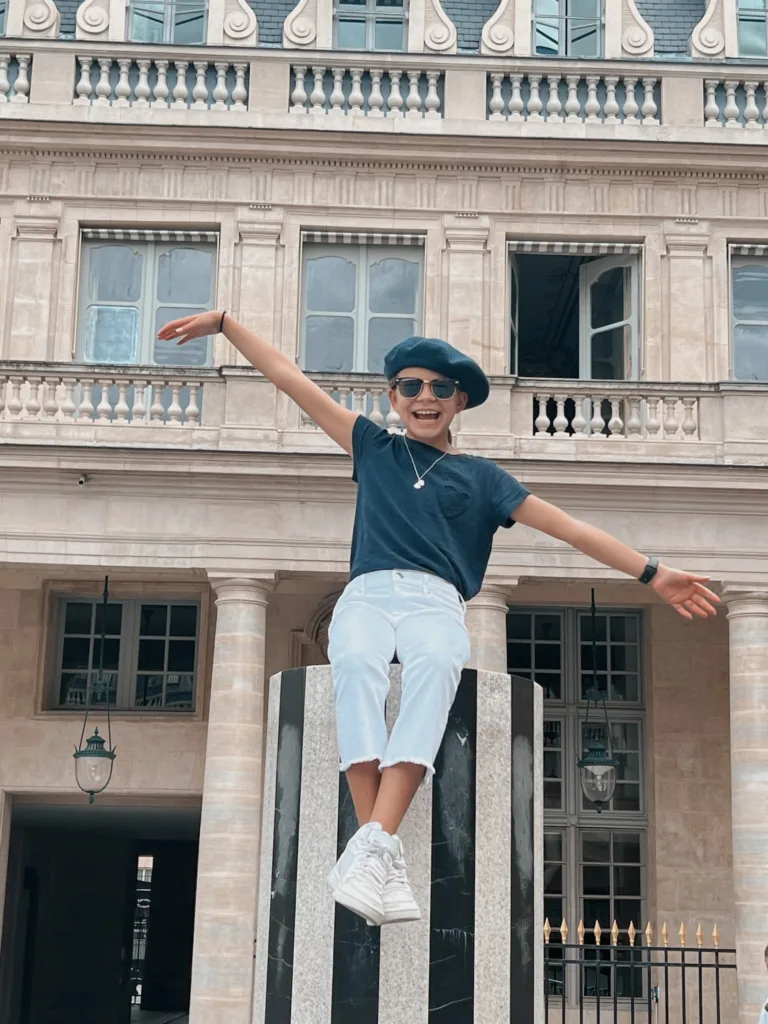 Girl in navy top and white jeans sitting on column of Palais Royal in Paris.