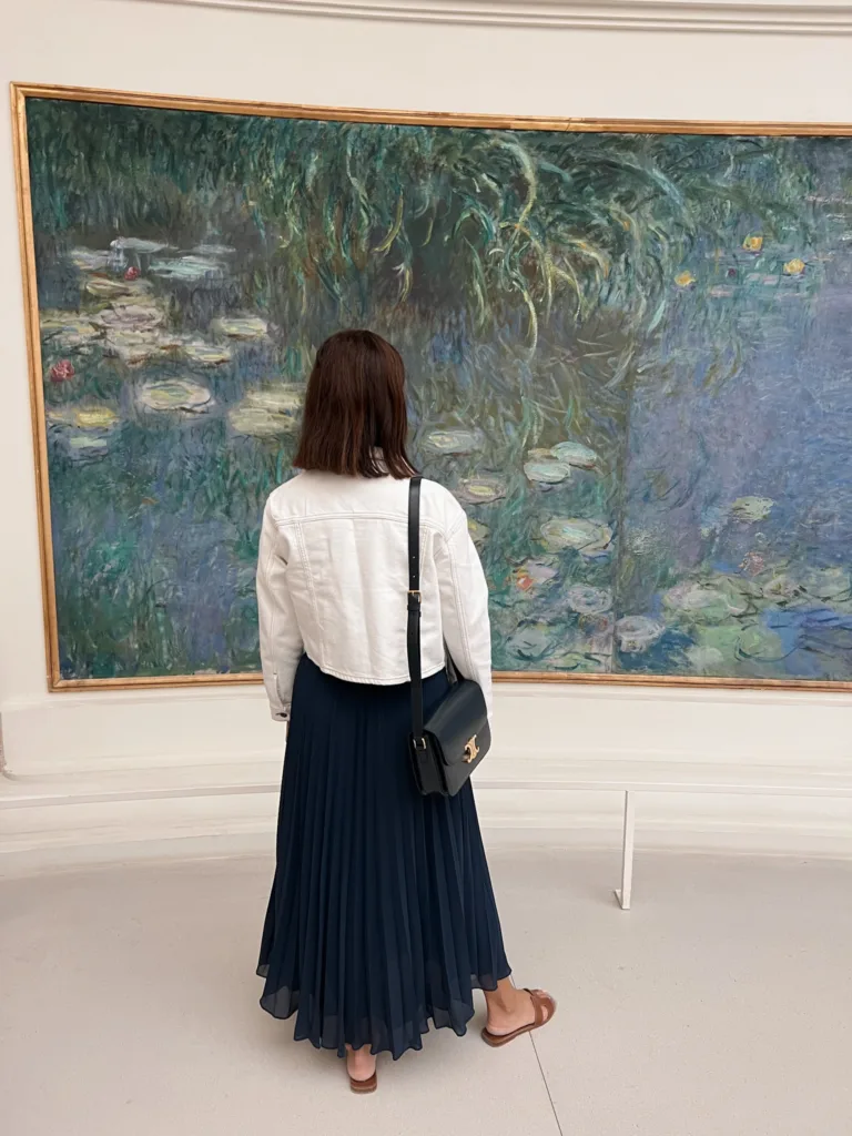 claude monet painting Woman in navy skirt with white jacket looking at picture of claude monet painting.