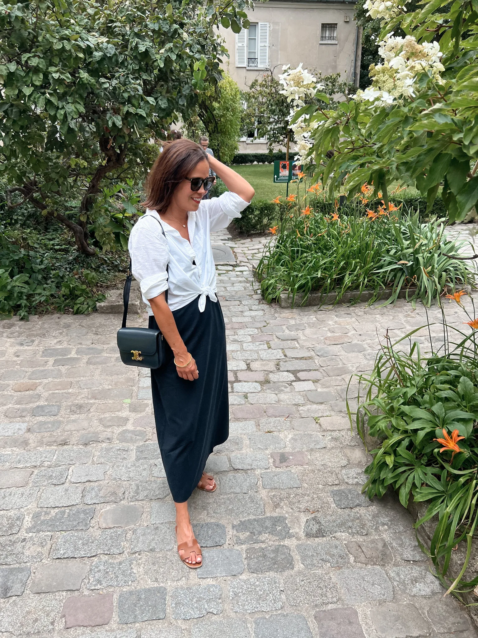Woman wearing navy skirt with white button down top standing by flowers.