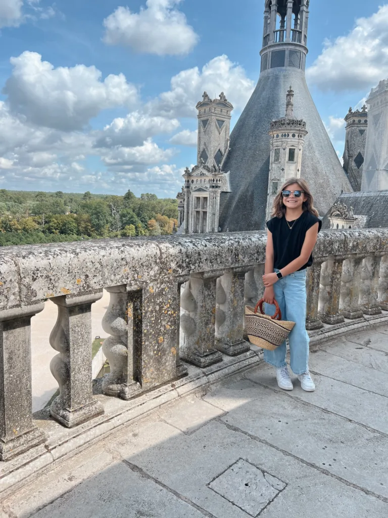Girl standing with basket bag in front of a castle.