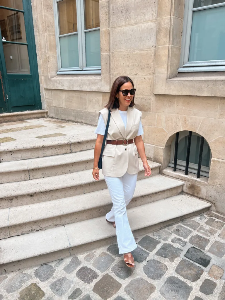 Woman wearing vest with white t-shirt and white jeans walking down stairs.