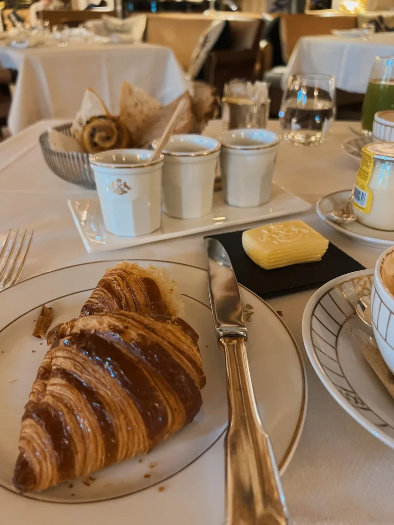 Picture of croissant on table with butter and 3 jam dishes.