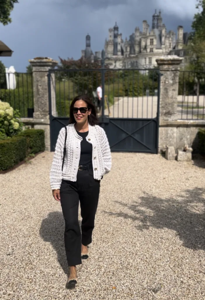 Woman walking wearing cardigan with black pants and castle in background.