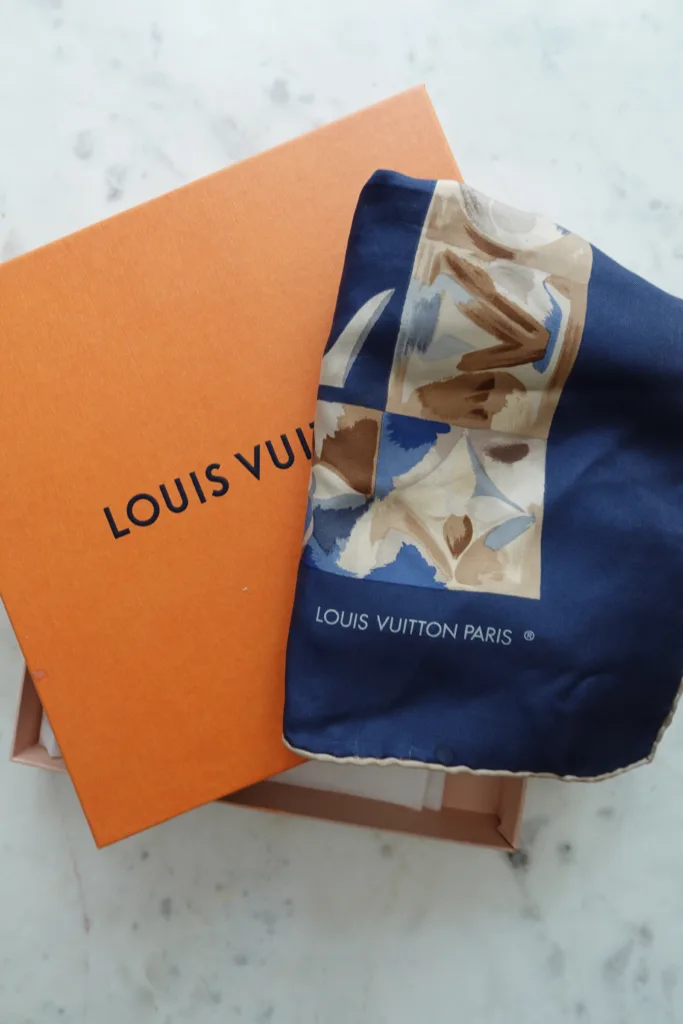 Louis Vuitton blue and brown scarf with the orange box on a table.