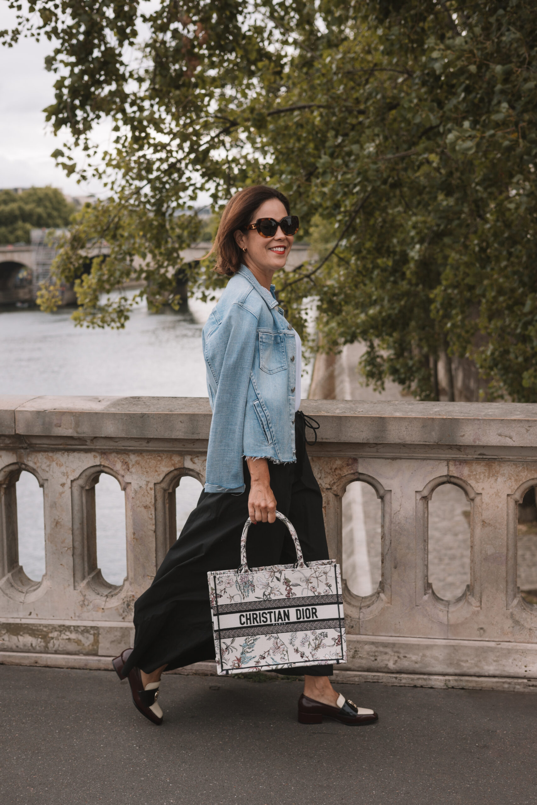 Woman wearing tote and denim jacket with loafers.