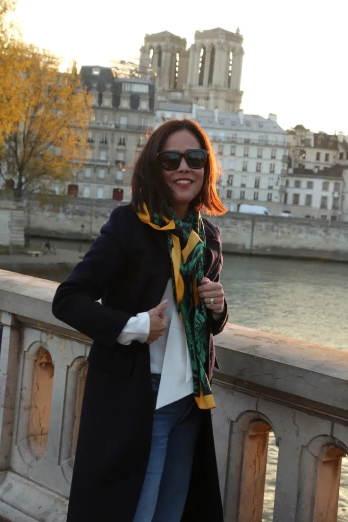 Woman wearing blue and yellow scarf next to seine in paris for what to pack for paris in the fall.