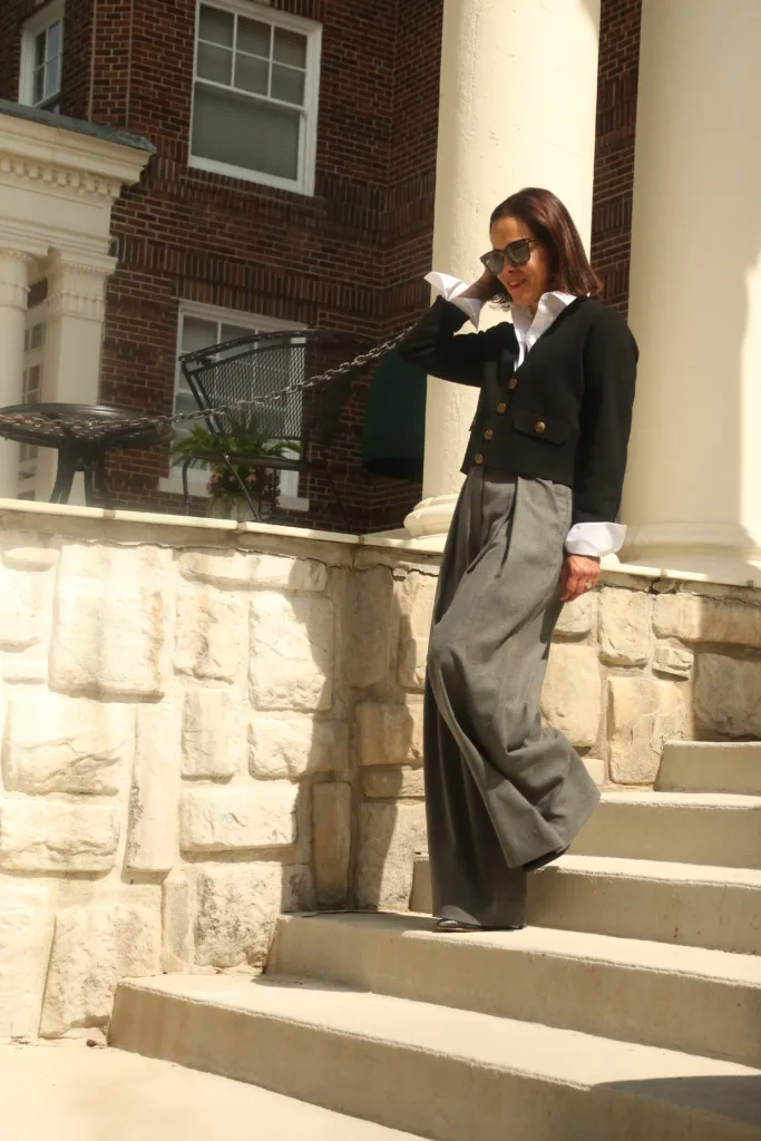 Woman walking down steps wearing grey trousers, black cardigan and white button down.