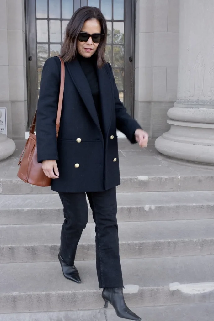 woman walking down the steps wearing a navy blazer and black denim.