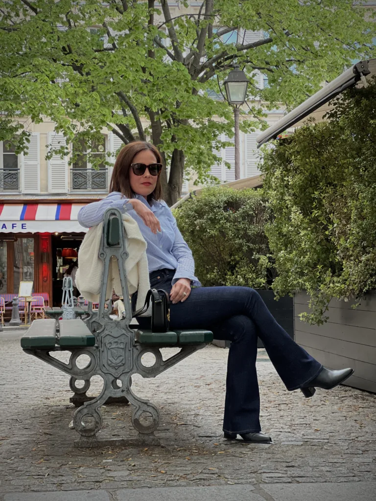 Woman sitting wearing blue and white striped top with dark jeans on a bench in Paris.