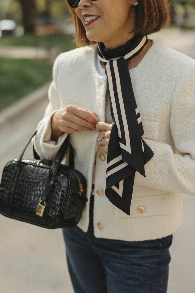 Woman holding black and white scarf with tweed jacket and black bag.
