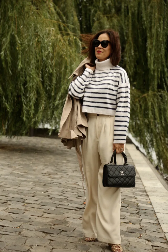 Woman wearing stripe sweater with cream pants and black bag for parisian brunch outfits in Paris.