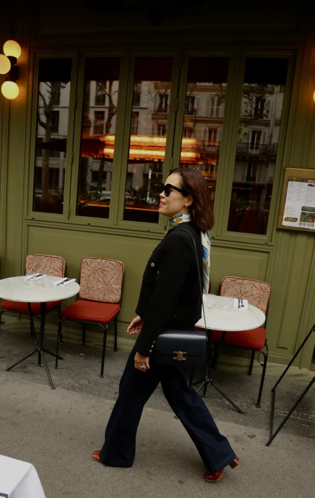 Woman wearing dark jeans in front of a restaurant in Paris for Parisian brunch.