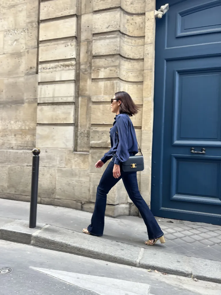 Woman walking in Paris in dark denim with navy silk shirt and gold sandals.