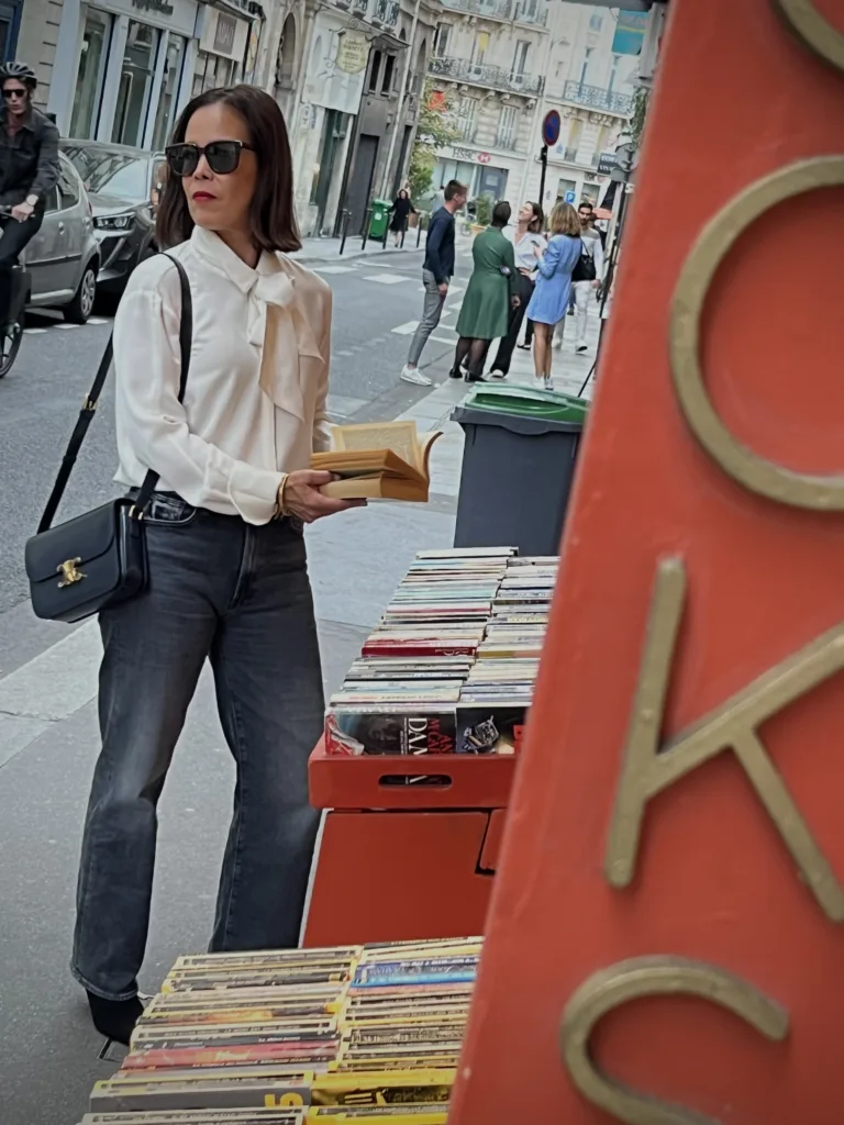 silk top and black jeans and sunglasses Woman looking at books wearing silk top and black jeans and sunglasses.