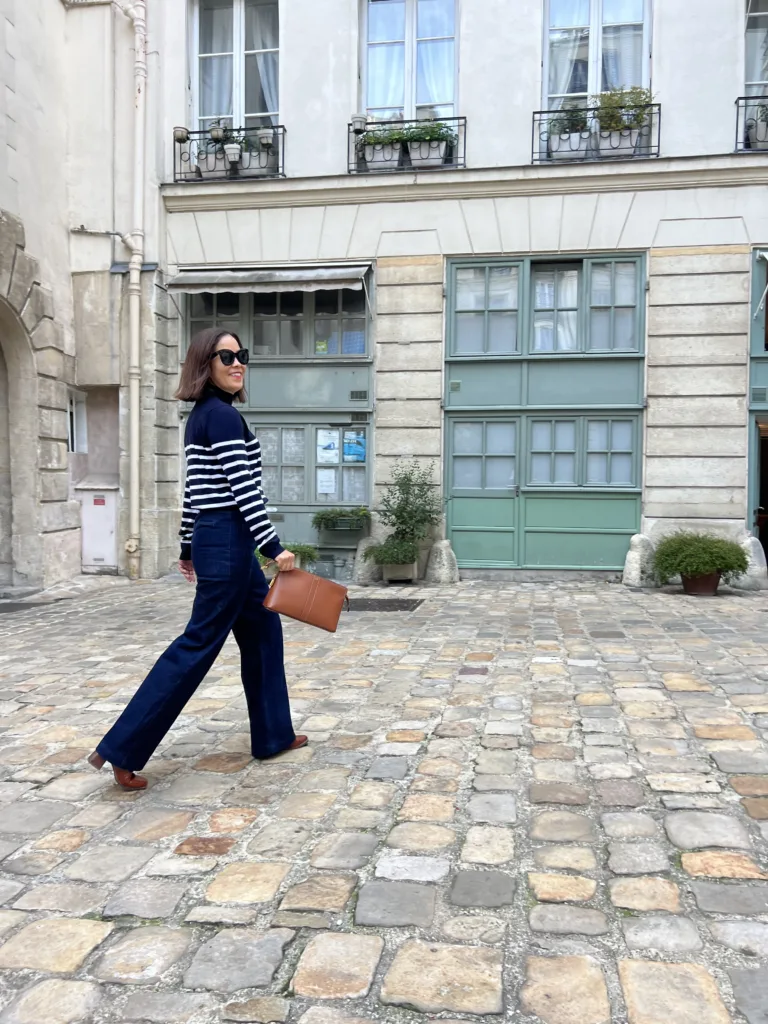 Woman wearing stripe turtleneck with high rise denim and boots in Parisian courtyard.