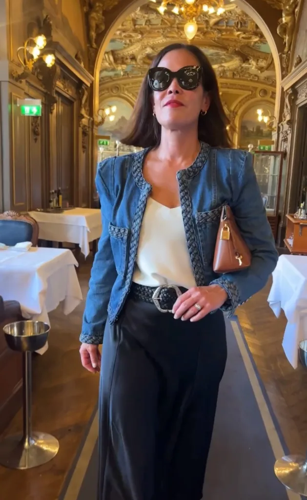 denim jacket and maxi skirt outfit Woman wearing denim jacket and silk cami with black skirt and tall boots in parisian restaurant.