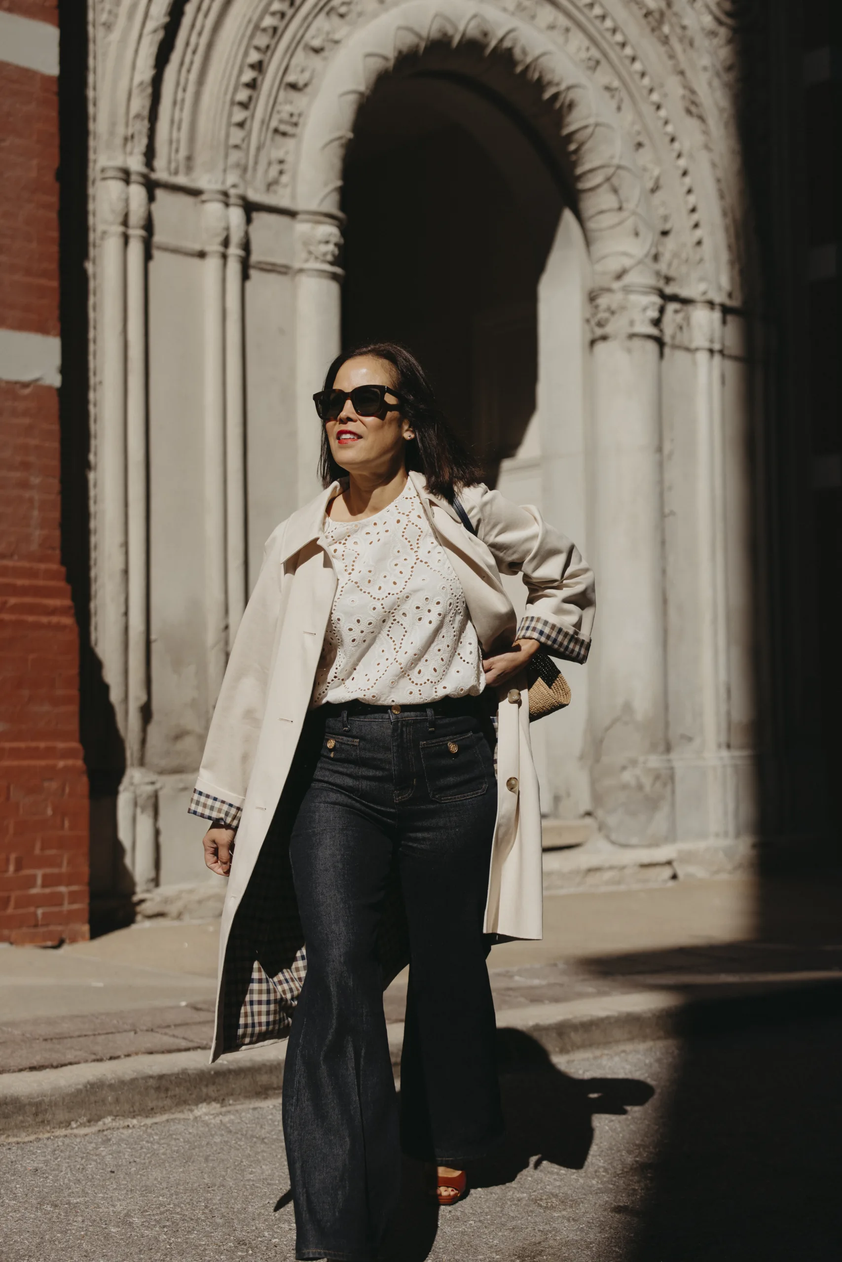 Woman wearing sezane light trench coat and dark denim walking across the street.