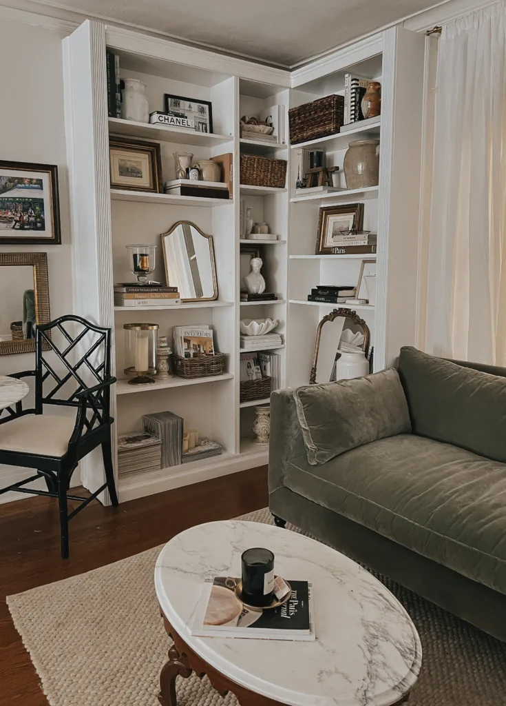 Green velvet sofa with black chair and bookshelf in living room.