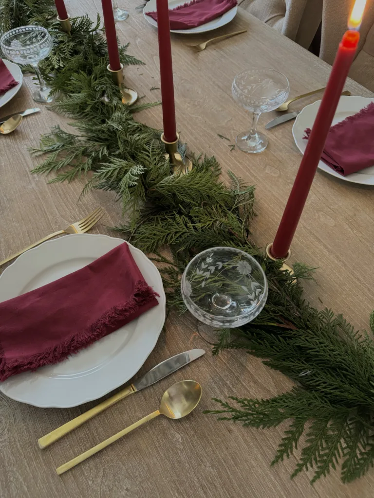 French holiday table Dining table with red candles, greenery, and white plates.
