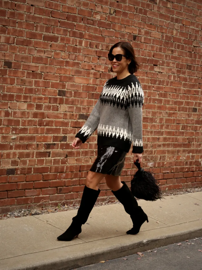 Holiday chic woman in sequin skirt and sweater with boots walking.