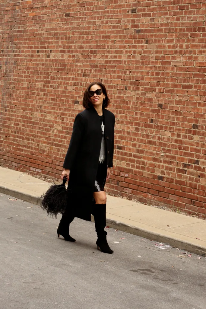 Woman in black coat, tall boots and skirt for holiday chic with j.crew walking down the street.