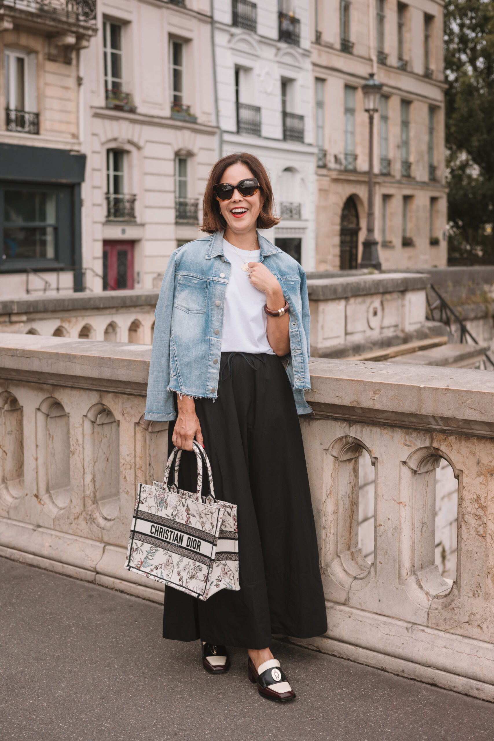 Woman holding Christian Dior book tote while standing on a bridge in Paris.