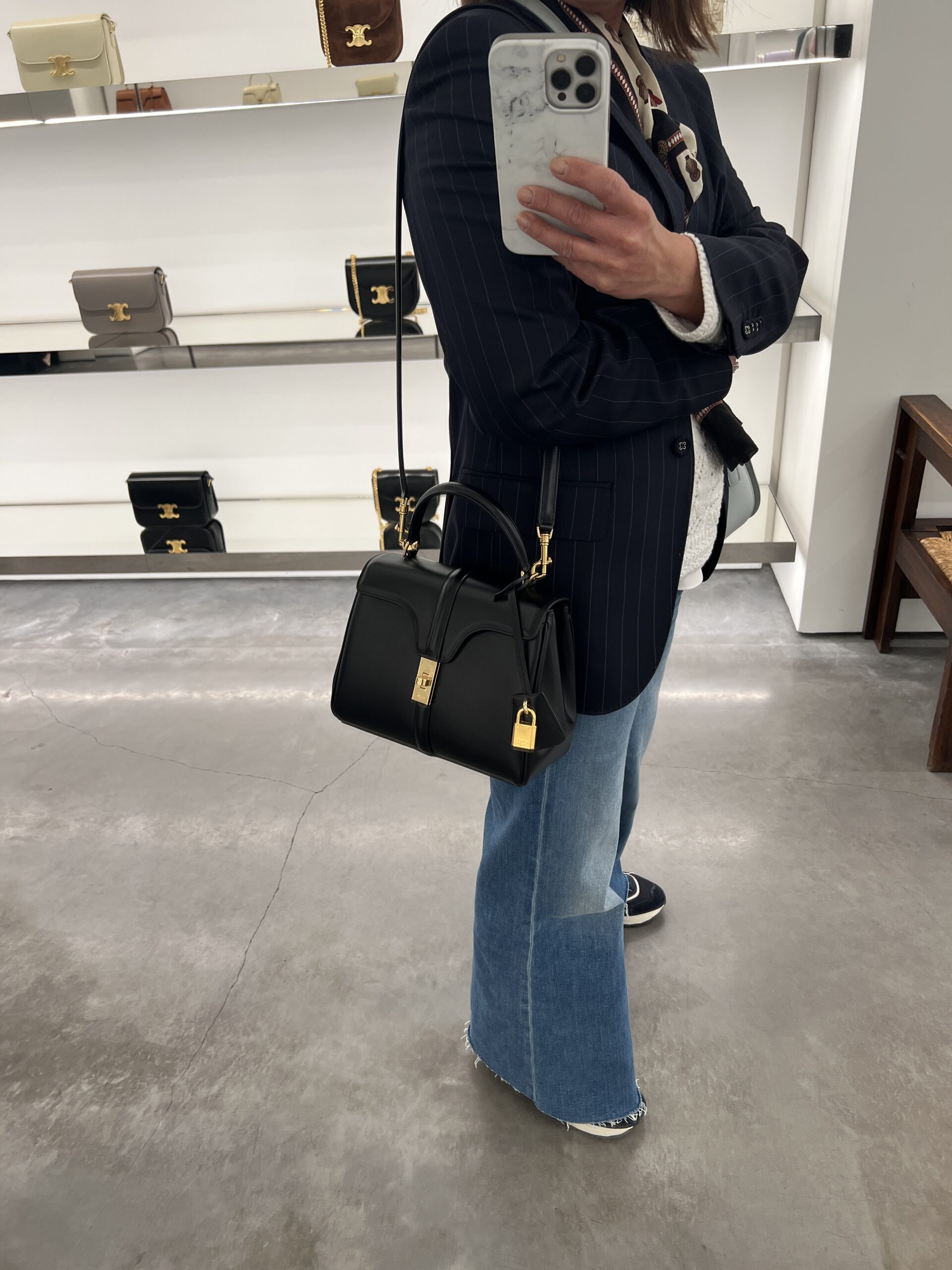 Interior of a Celine store in Paris with a variety of handbag styles and a woman holding a Celine 16.