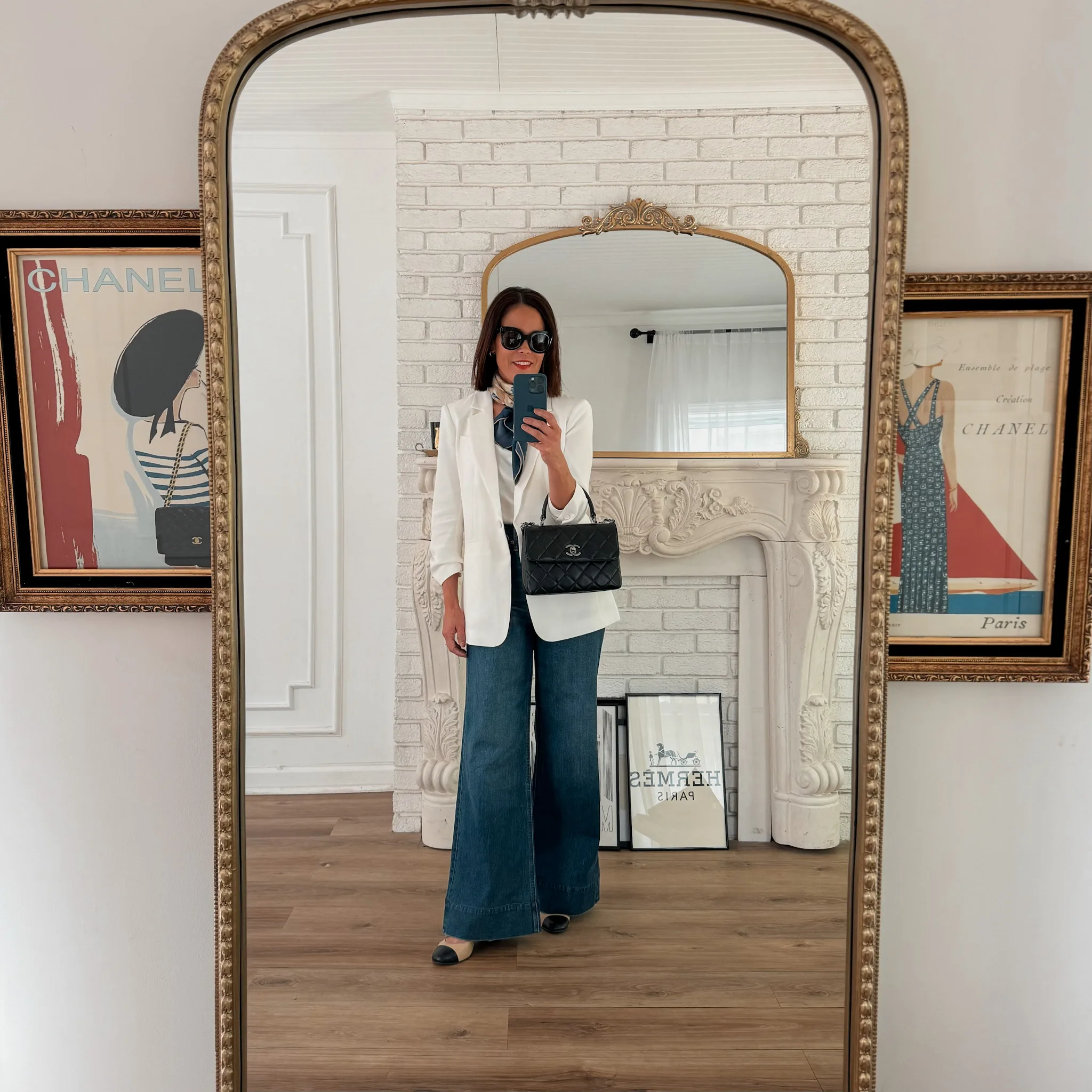 Woman in white blazer with flare denim and black handbag taking a selfie.