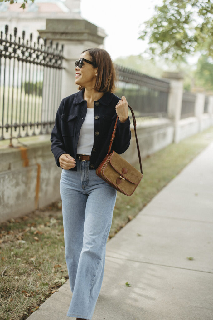 Woman wearing navy cardigan walking with denim and purse.