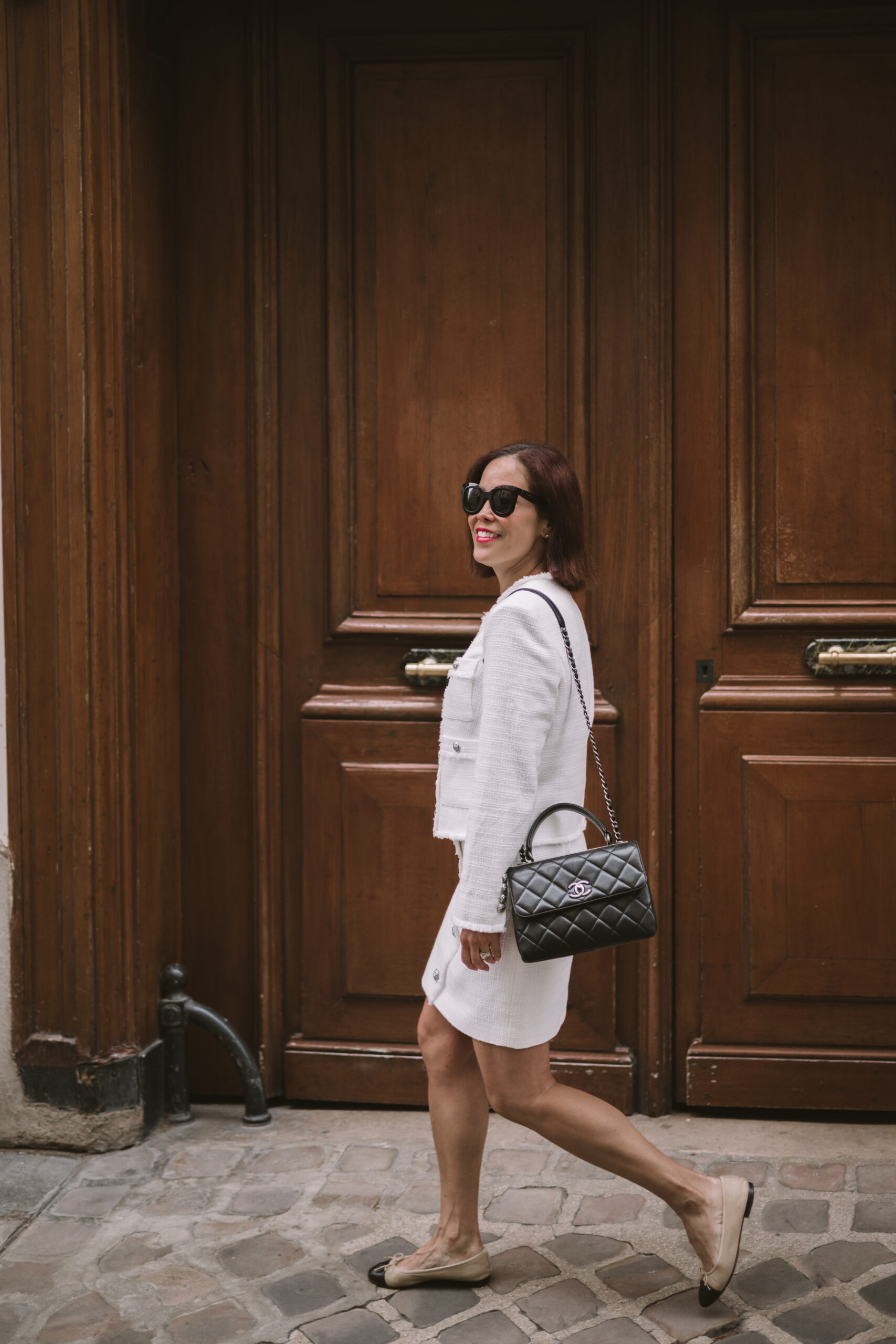 Woman wearing tweed jacket and matching skirt in Paris walking in front of a brown door.