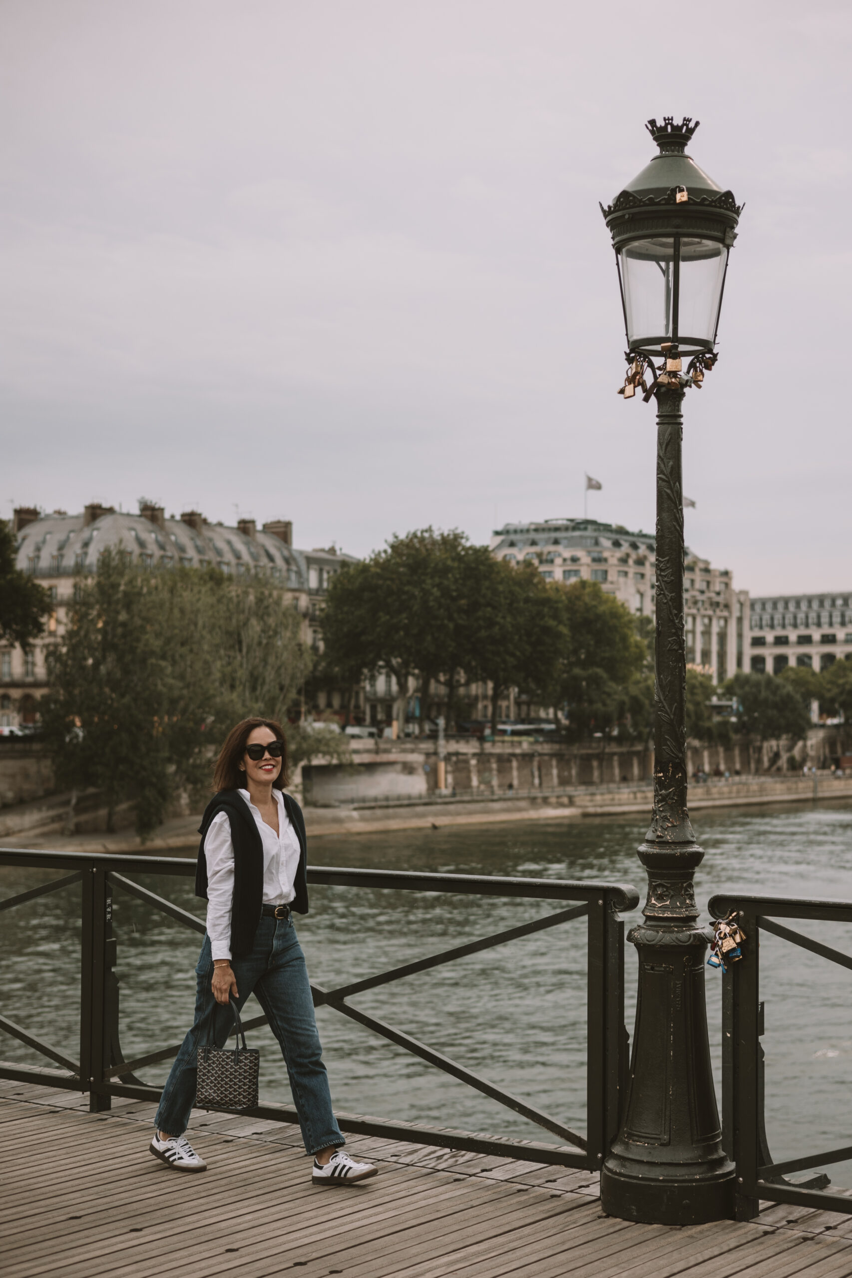 Woman wearing jeans, sneakers, walking across bridge in Paris during fall.