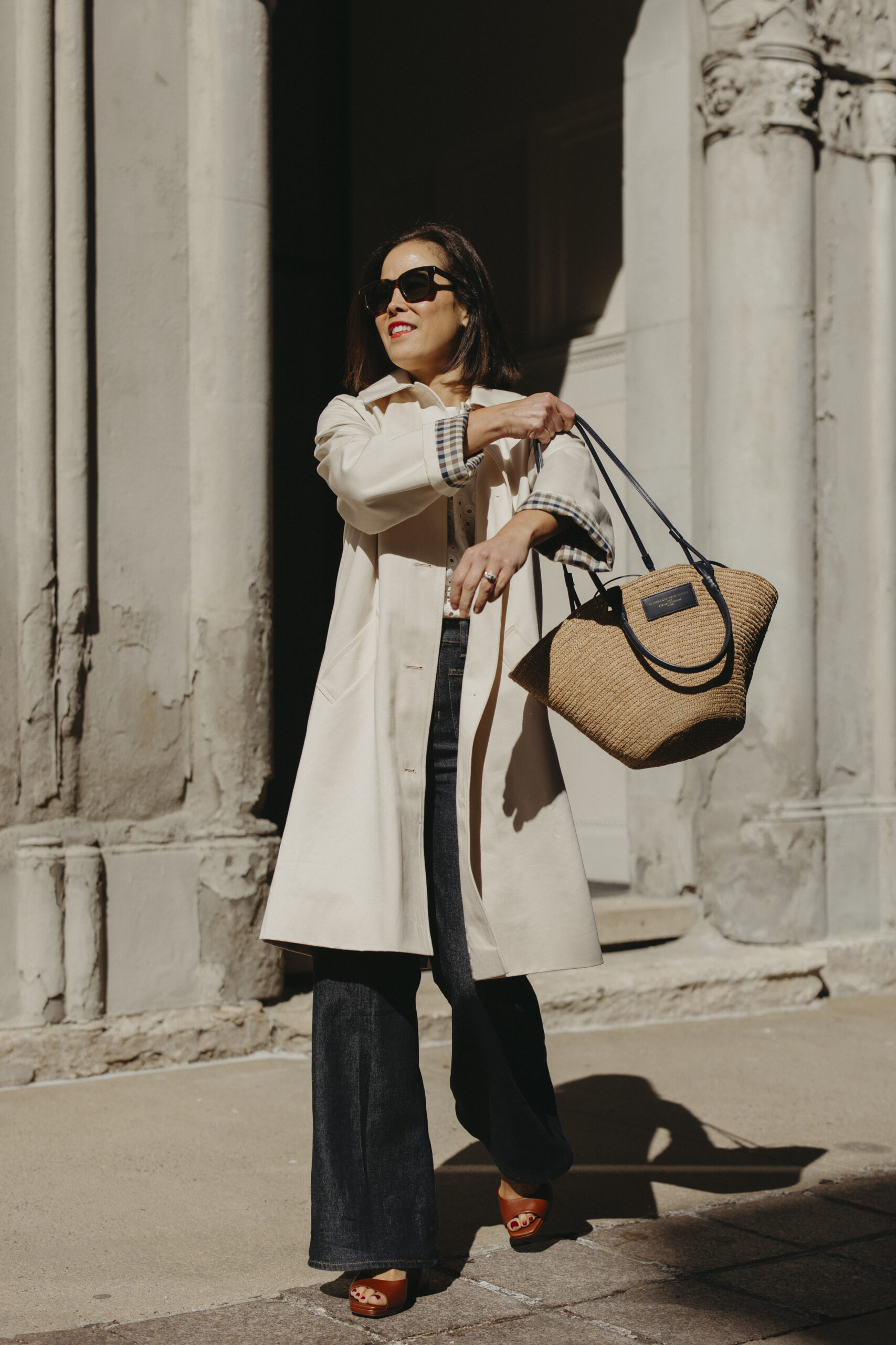 Woman wearing trench coat with dark denim, basket bag, for spring.