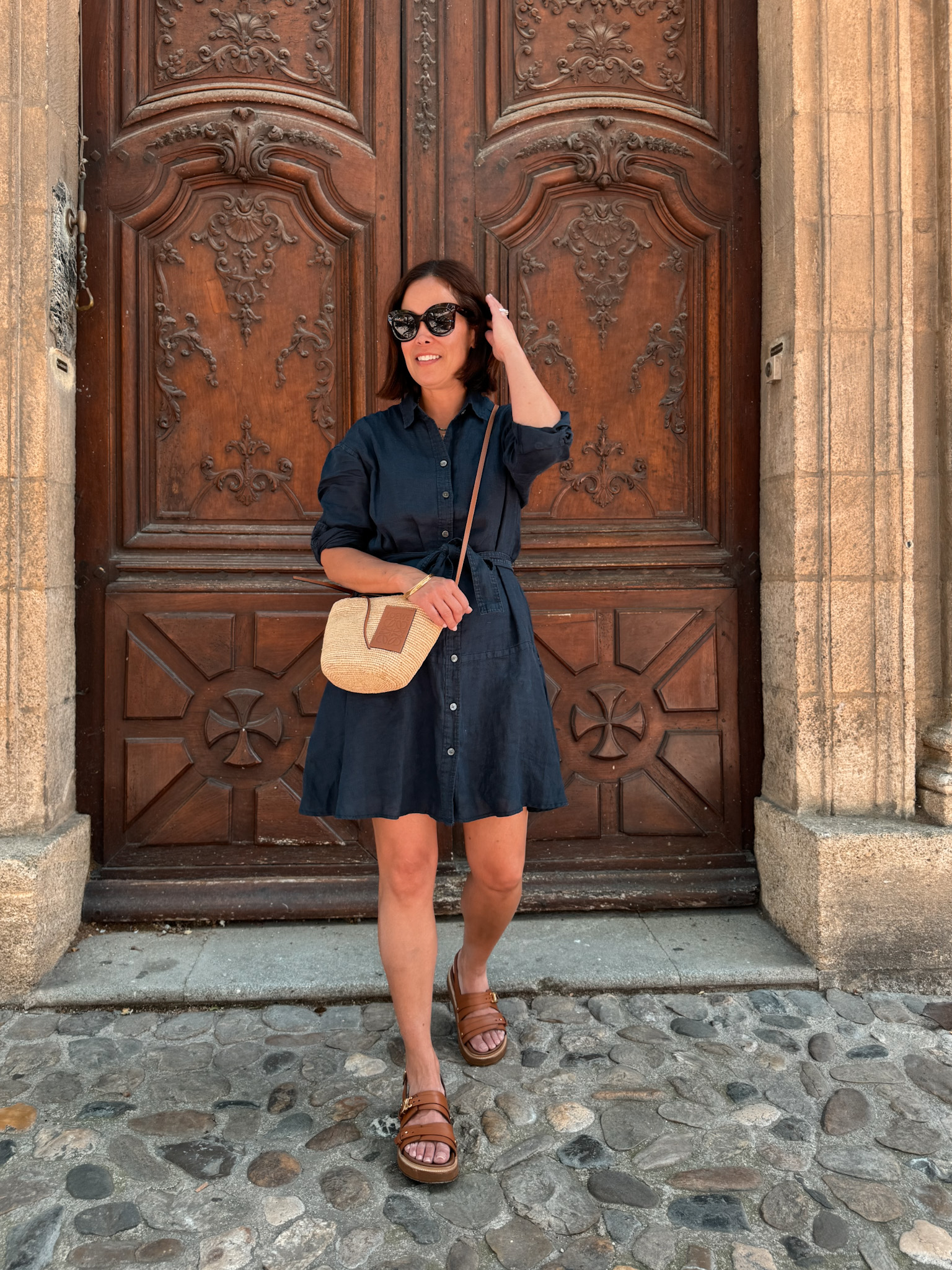 woman in navy linen dress wearing brown sandals and small bag.