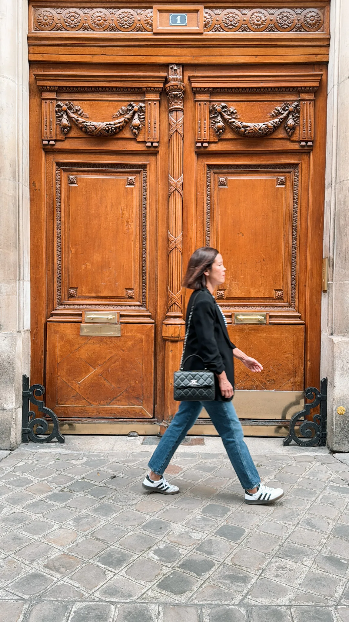 Woman walking past big brown doors in Paris.