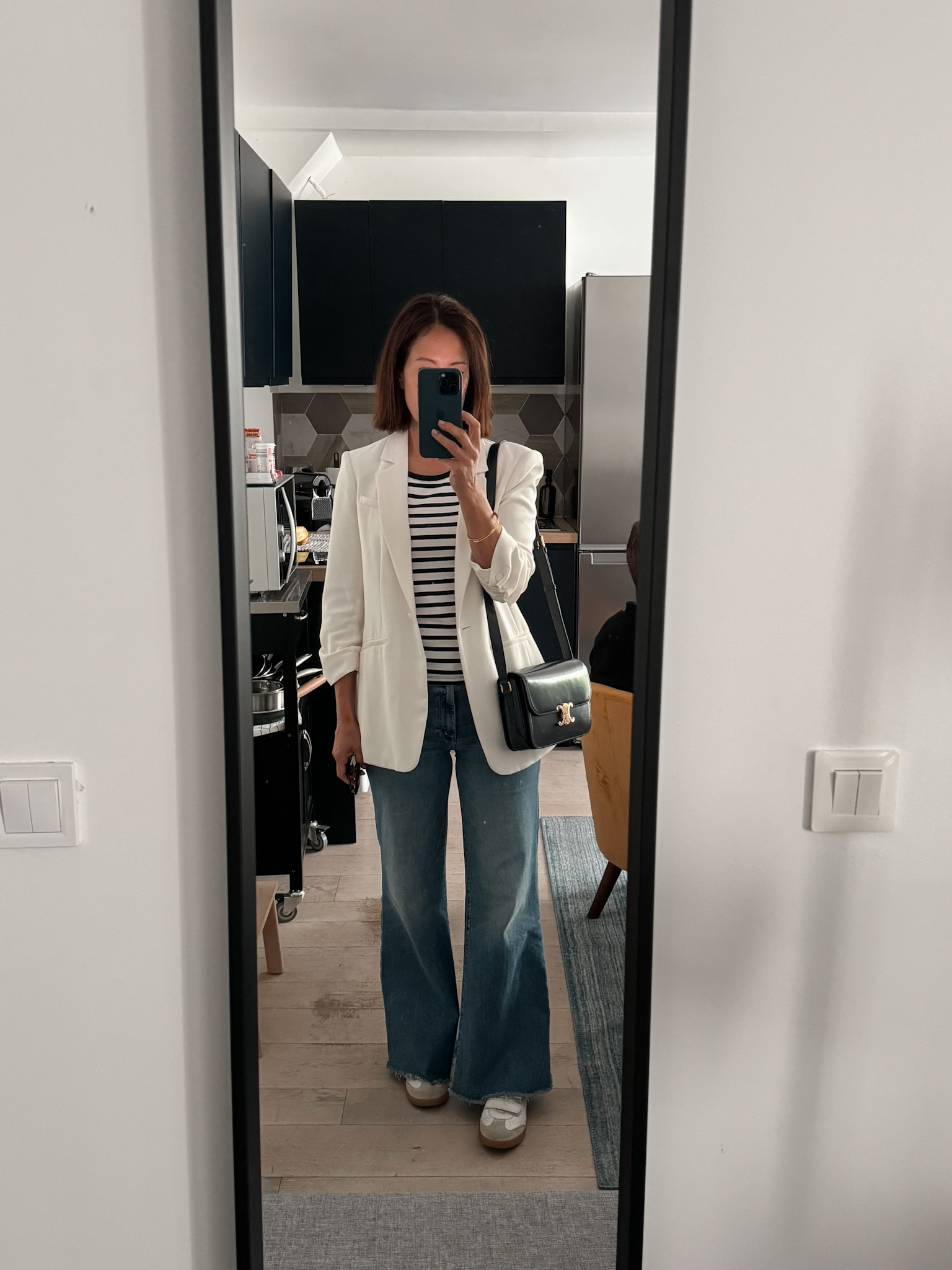 Woman wearing white blazer with flare denim and stripe top.