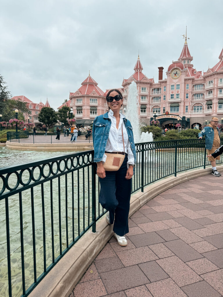 Woman wearing denim jacket with navy pants standing on a fence at Disneyland.